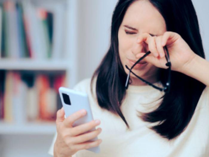 Una imagen que muestra a una mujer de unos 30 años mirando su teléfono mientras se frota los ojos.