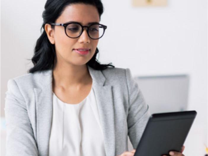 Una imagen de una mujer mirando la pantalla de una tablet con los lentes puestos.