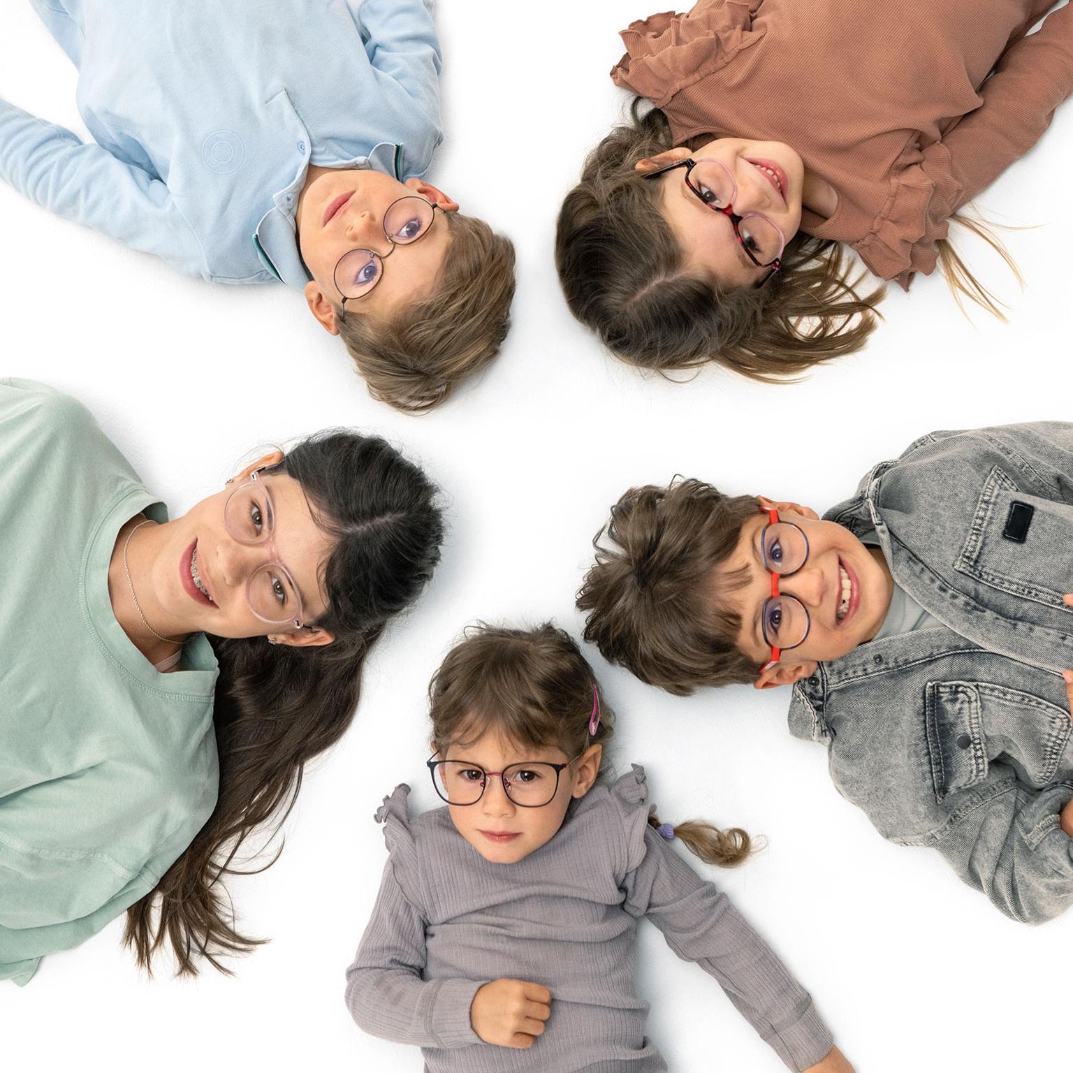 Grupo de niños con lentes, tendidos alegremente en círculo sobre el suelo