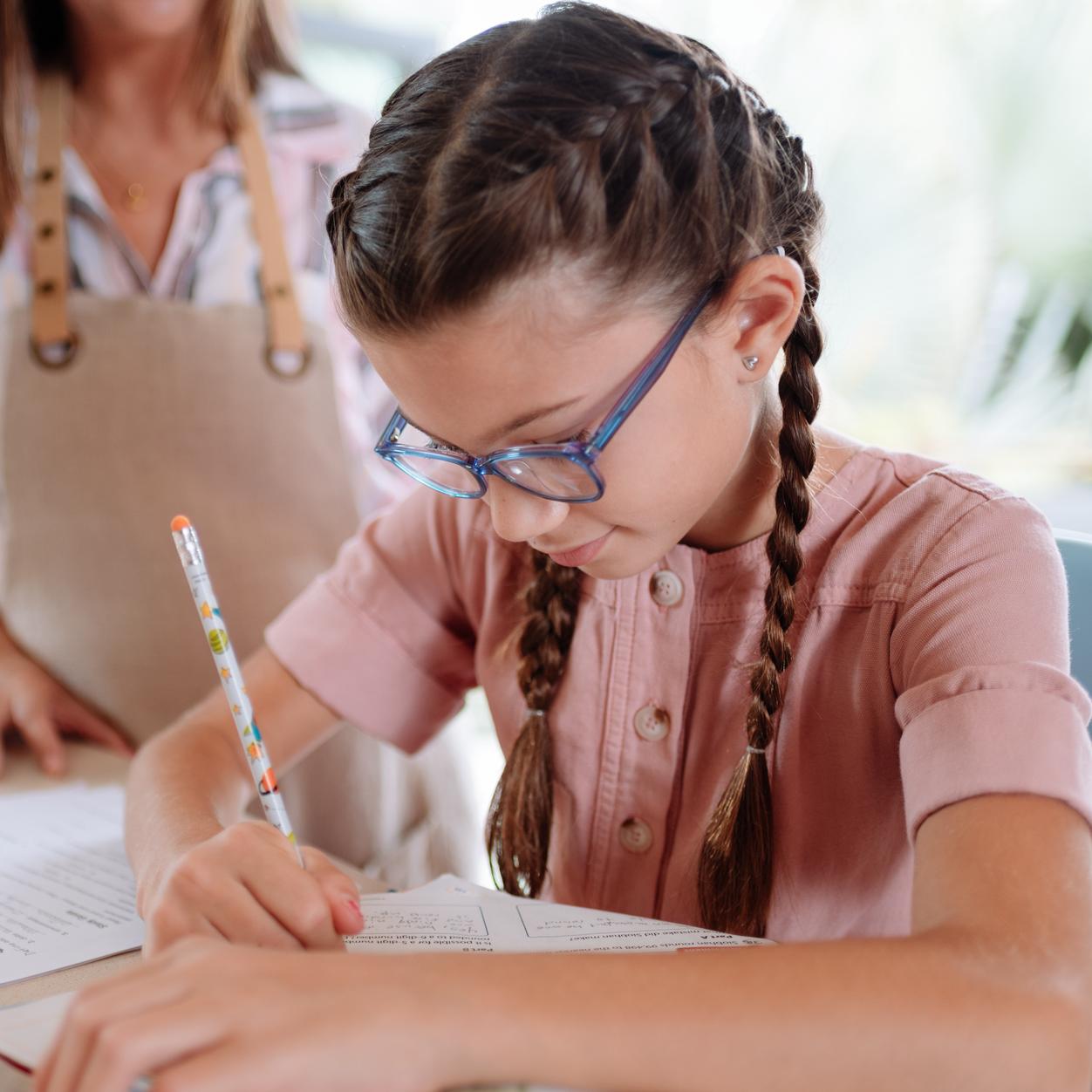Niña con lentes que escribe con bolígrafo