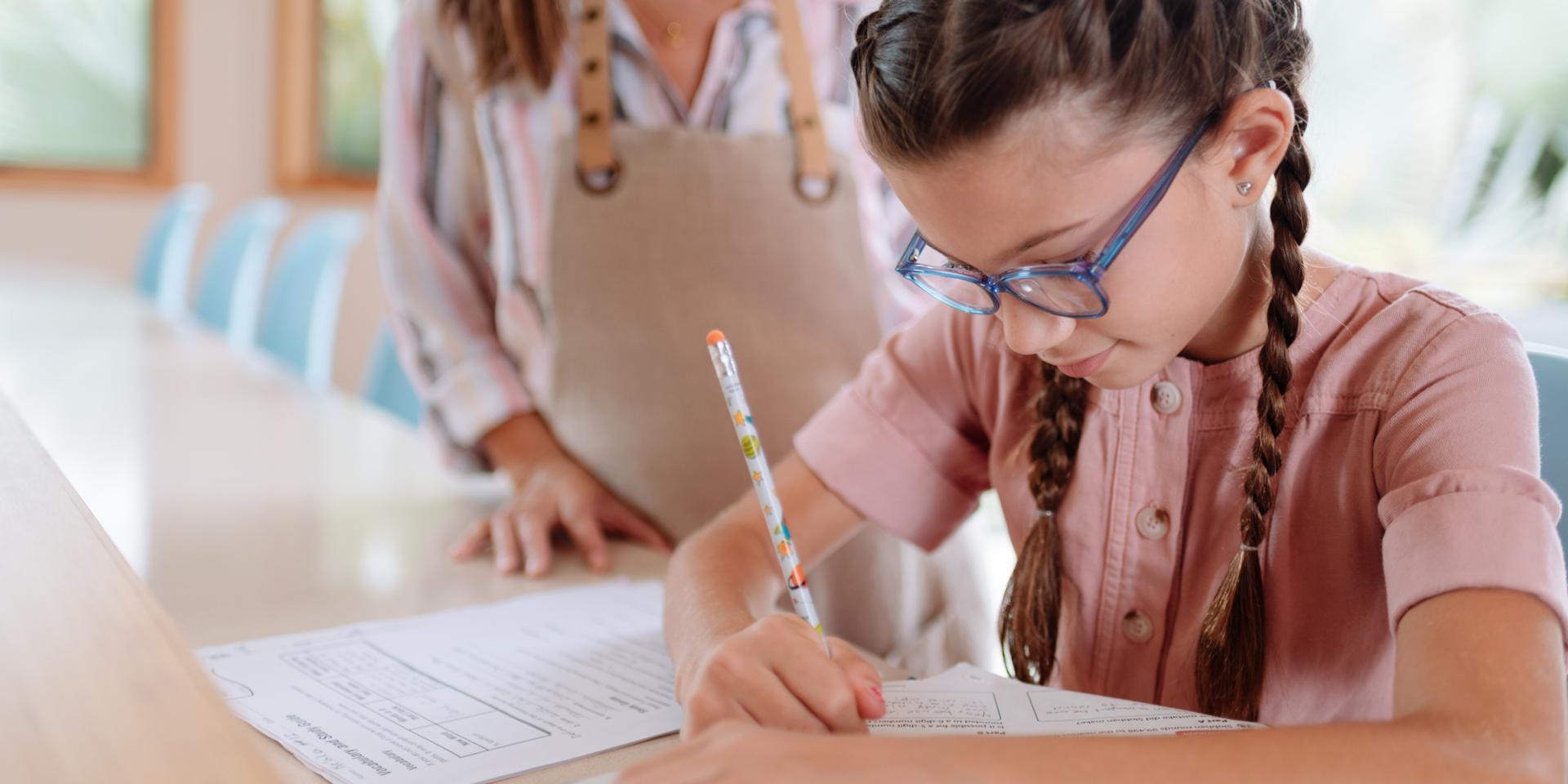 Niña con lentes que escribe con bolígrafo