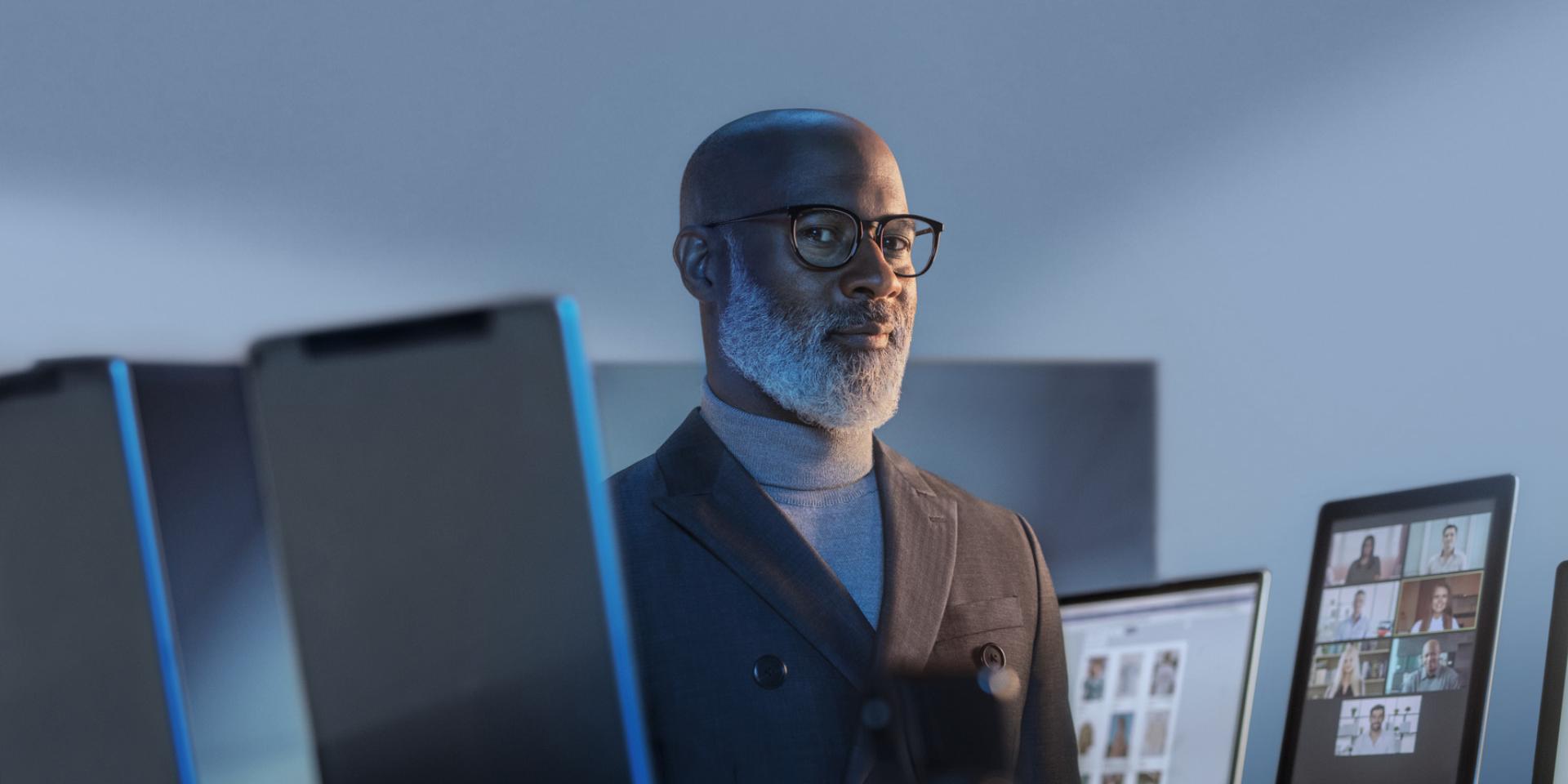 Hombre sonriente rodeado de dispositivos digitales usando lentes ZEISS BlueGuard para protegerse de la luz azul.