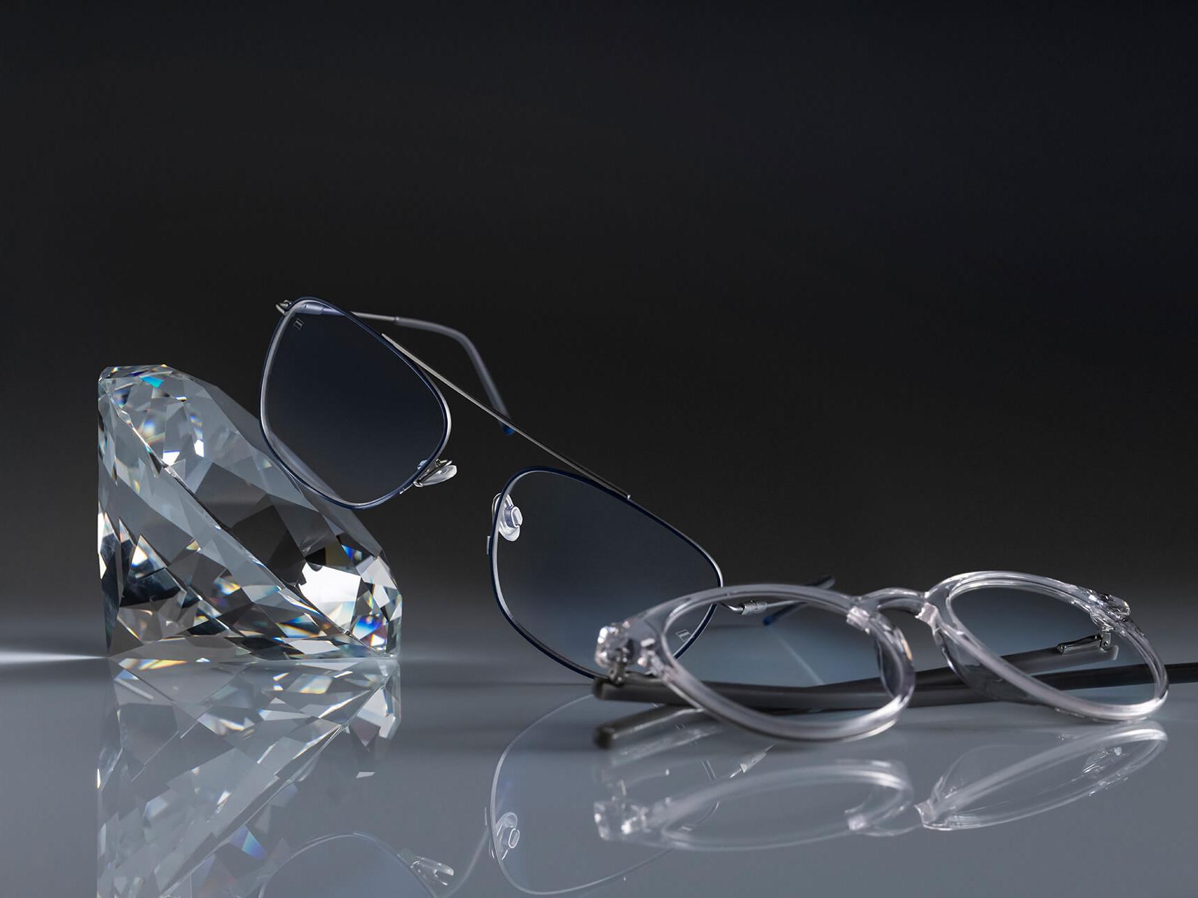 Dos pares de lentes con lentes ZEISS y el recubrimiento ZEISS más duro jamás visto: DuraVision® Platinum. Un par de lentes apoyado en un cristal, el otro sobre el suelo. Ambos tienen lentes transparentes sin reflejos azulados.