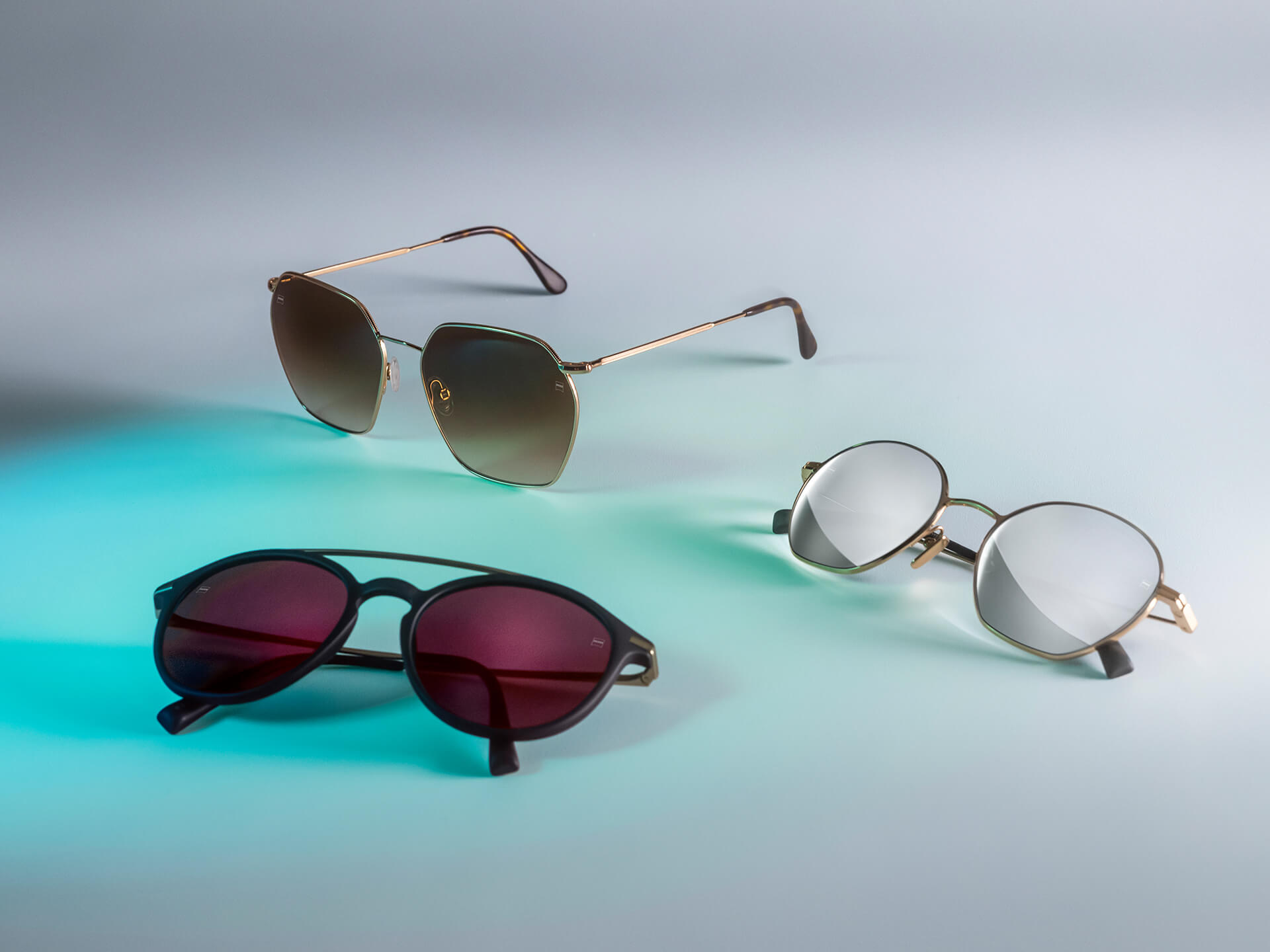 Tres pares de lentes de sol con lentes de lentes de sol ZEISS de distintos colores, con recubrimientos DuraVision Sun, DuraVision Mirror y Flash Mirror, visibles sobre un fondo blanco con reflejo de luz azul.