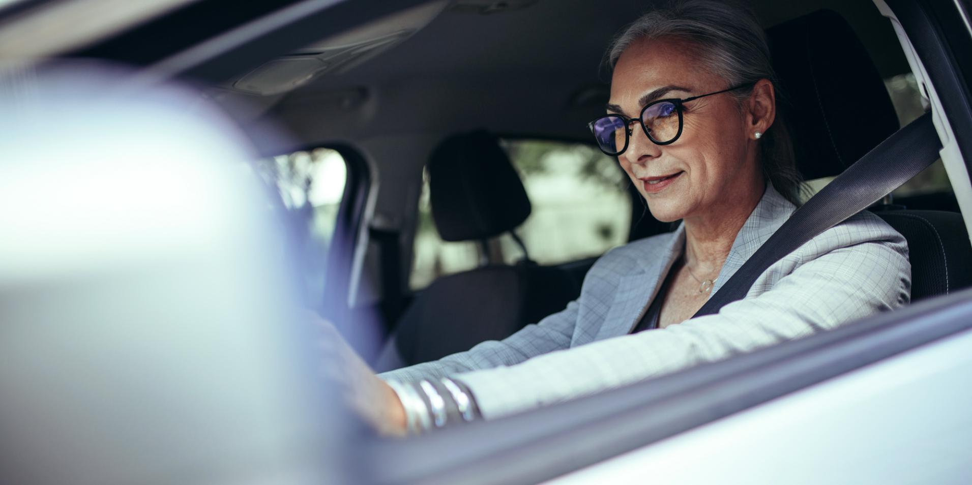 Una mujer madura en un vehículo usa lentes con lentes ZEISS DriveSafe.
