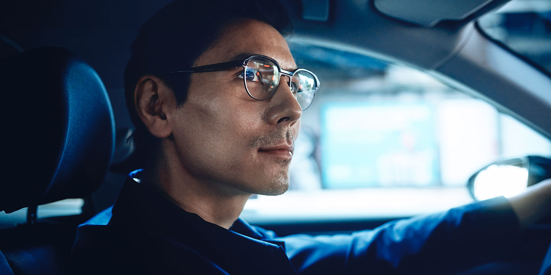 Hombre conduciendo un vehículo, seguro de sí mismo, y con una ligera sonrisa. Usa lentes de visión sencilla ZEISS DriveSafe.