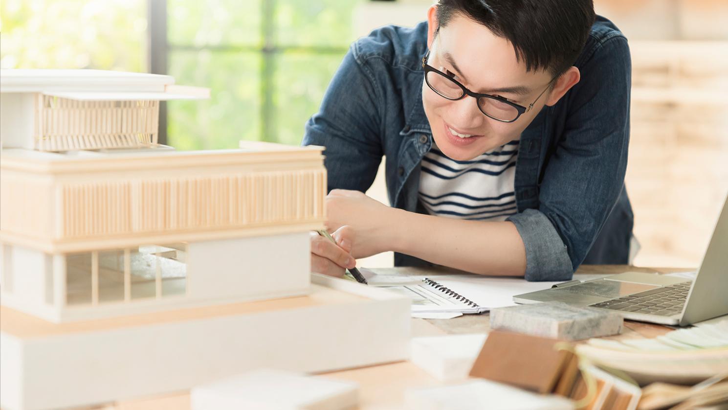Hombre de mediana edad con pelo corto negro y lentes de oficina ZEISS Office para poder concentrarse en los detalles de un intrincado modelo arquitectónico. 
