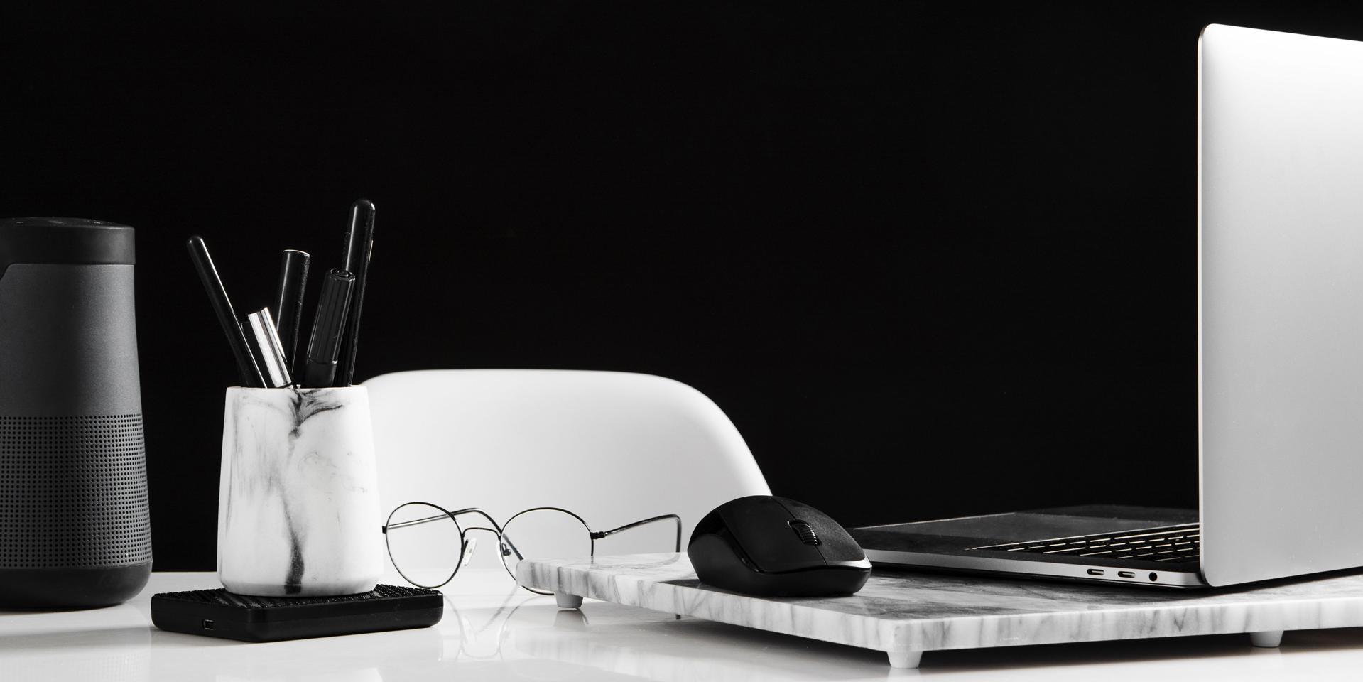Espacio de trabajo ordenado que muestra un portátil abierto en el lado derecho con un ratón. Justo delante, un par de lentes. A la izquierda de la imagen, hay un portalápices.