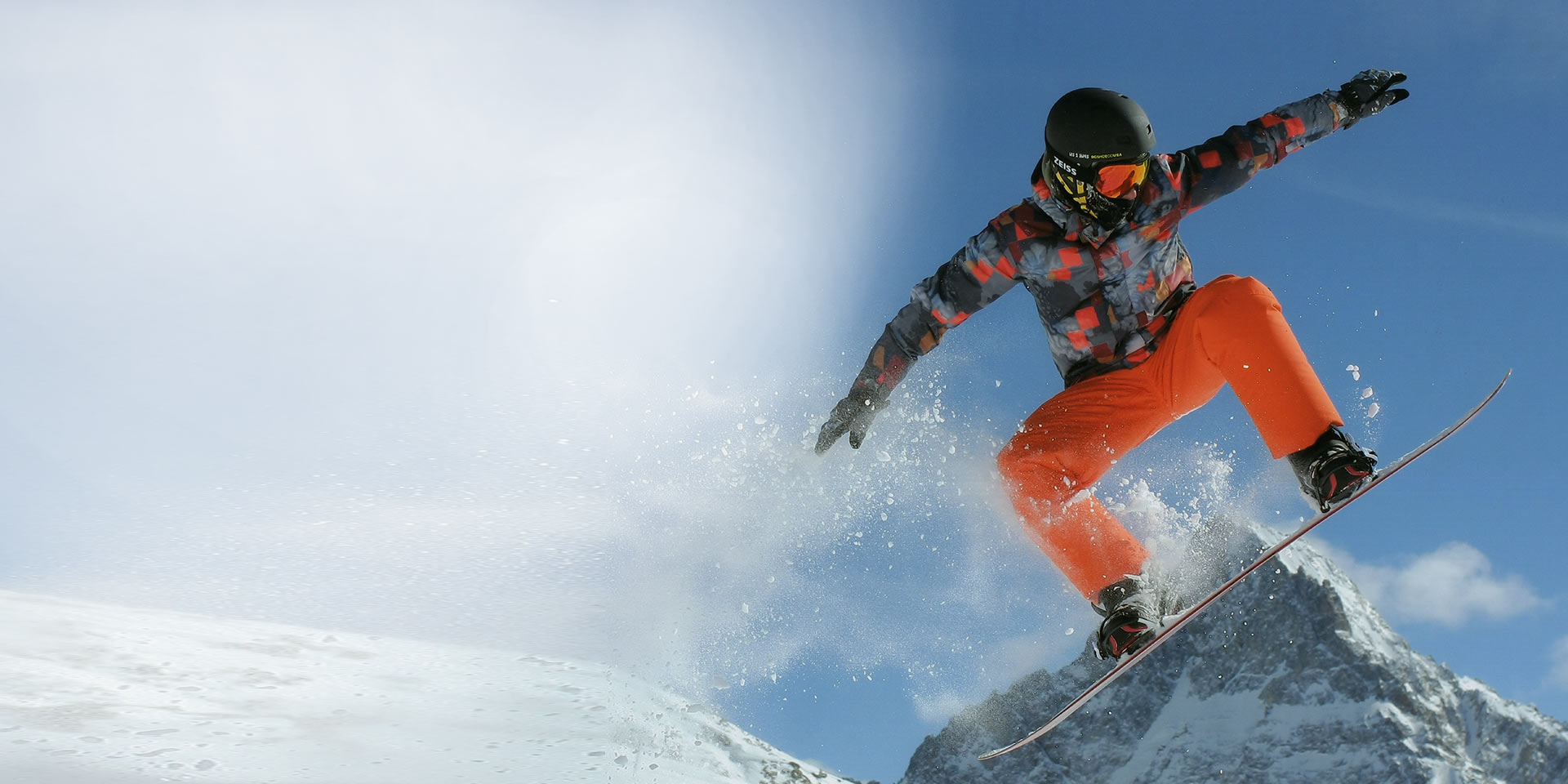 Un hombre salta con una tabla de snowboard, porta un casco de esquí negro y máscaras de nieve ZEISS con tecnología Interchargeable para protección