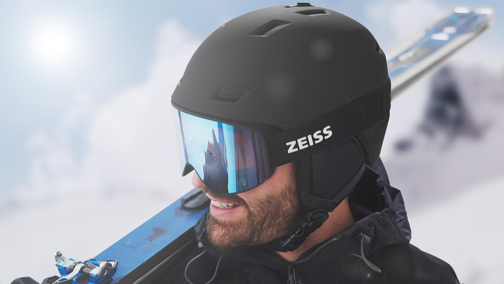 Un hombre, con los esquís sobre el hombro derecho, viste un casco negro con máscaras de esquí ZEISS azules espejadas.