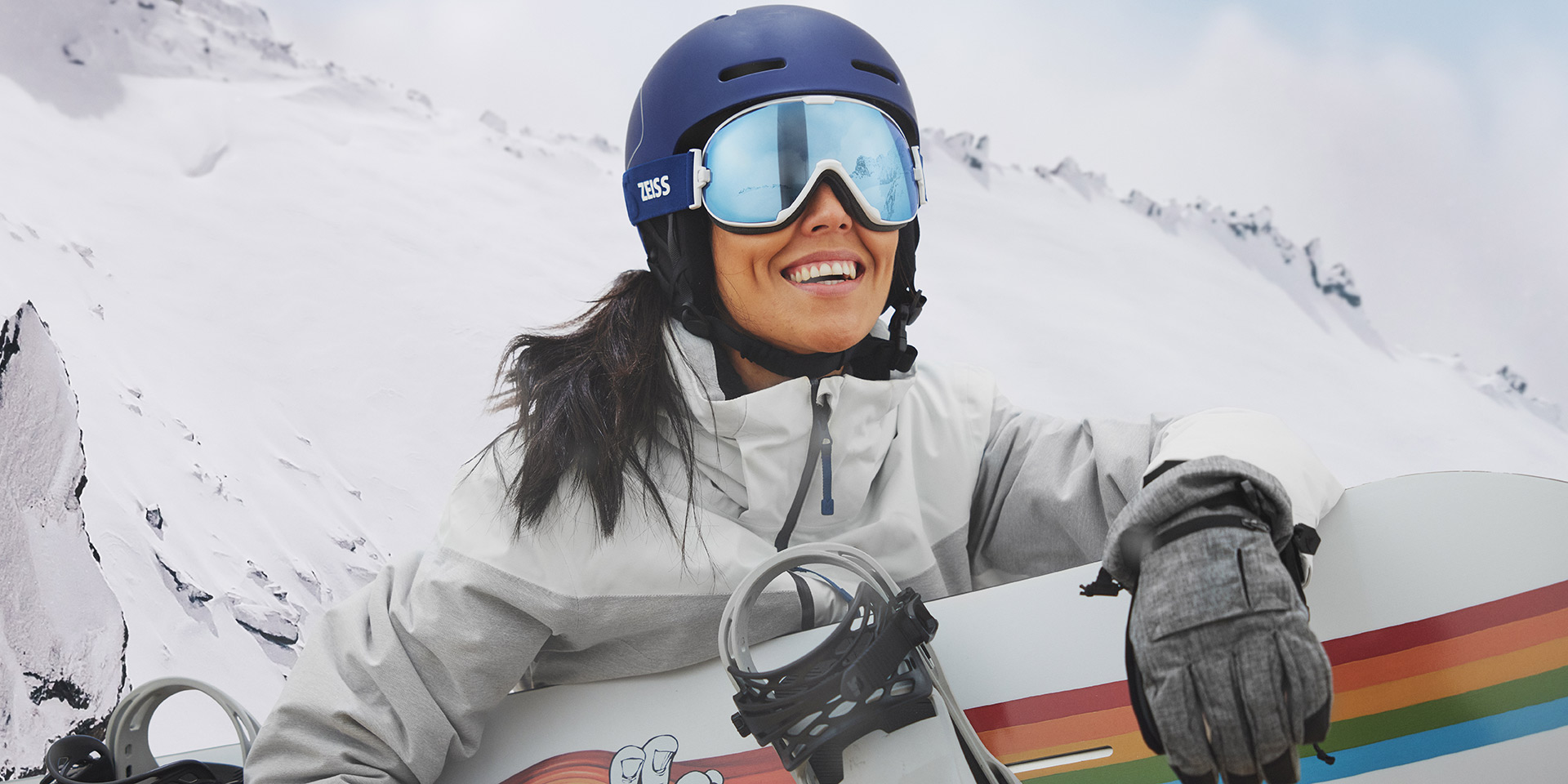 Una joven mujer luce goggles de nieve con tecnología ZEISS Interchangeable y sujeta una tabla de snowboard.