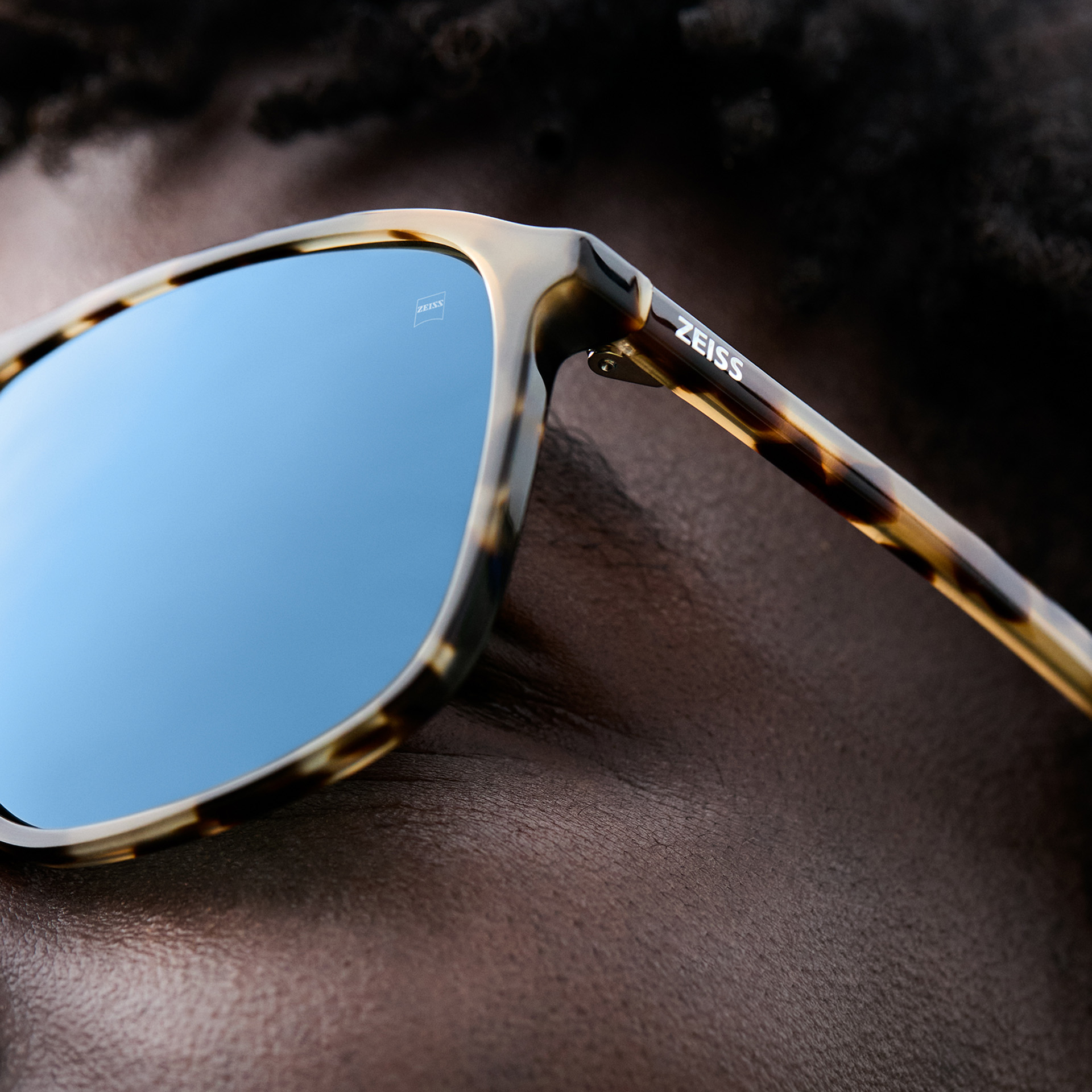Primer plano de un hombre con gafas de sol de caparazón de tortuga con lentes que reflejan el cielo azul.